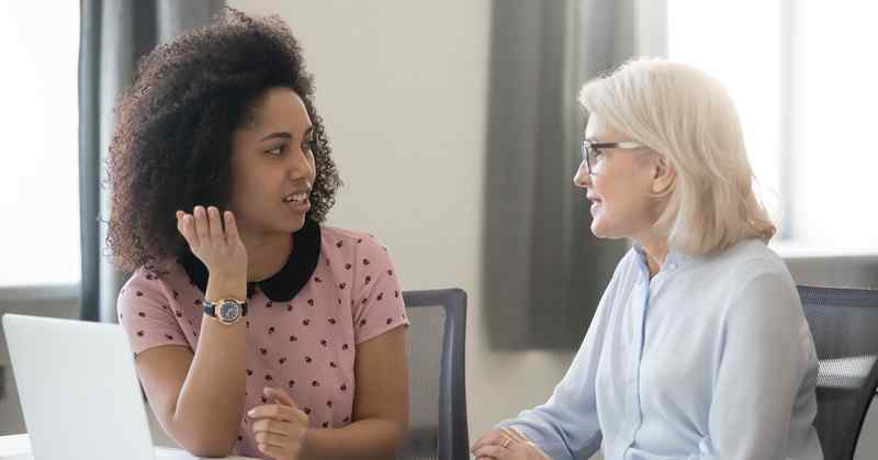 Two women at a table, with an open laptop, having a discussion